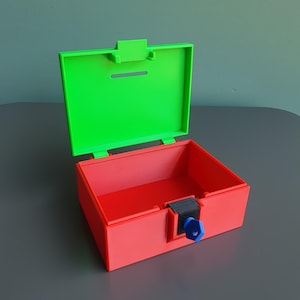 May include: A rectangular red plastic box with an attached bright green lid that features a horizontal slot. The box includes a black locking mechanism on the front with a small blue key inserted into the centre, allowing the container to be secured.