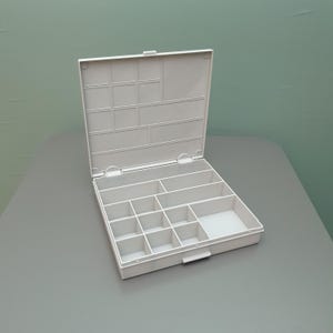 May include: A white plastic storage box with an attached hinged lid. The interior features multiple fixed compartments of varying sizes, including several small square sections and two larger rectangular sections, designed for organizing small items.