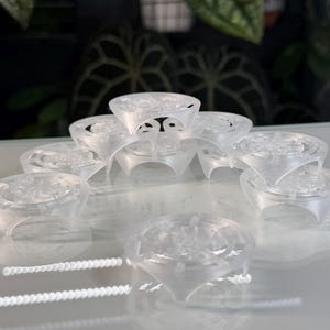 Puede incluir: Anillos transparentes y claros con un diseño similar a un diamante. Los anillos están dispuestos en un patrón circular, mostrando sus intrincados detalles. El diseño parece estar impreso en 3D, con un enfoque en las formas geométricas. Probablemente sean joyas o artículos decorativos.