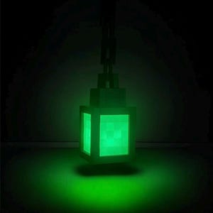 May include: A green, pixelated lantern with a glowing interior, suspended from a chain. The lantern's design is blocky, with a bright green light emanating from within. The background is dark, emphasizing the lantern's illumination.