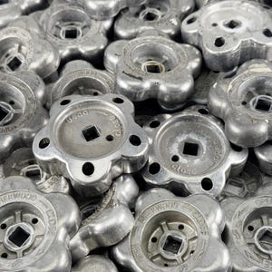 May include: A collection of silver-colored, flower-shaped valve handles. Each handle has a square center hole and the words "OPEN" and "CLOSE" are visible. The handles are made of metal and have a slightly worn appearance.