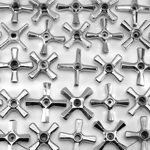 May include: A collection of shiny, chrome-colored faucet handles arranged on a white surface. Each handle has a four-arm design with a central hole. The handles are evenly spaced, creating a pattern. The image is in black and white.