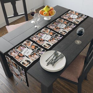 Peut inclure: Une nappe noire avec un collage de photos et les mots "Custom Text Here". La nappe est posée sur une table en bois sombre, avec des assiettes, des couverts et des verres à vin. Un bol de pommes est également sur la table.