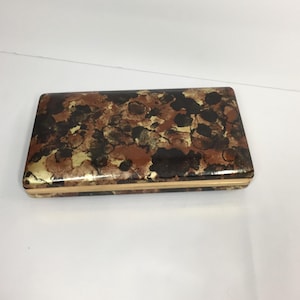 May include: Rectangular box with a decorative pattern in shades of brown, black, and gold. The box has a glossy finish and a gold-colored trim around the edges. The pattern appears to be abstract, with irregular shapes and textures.