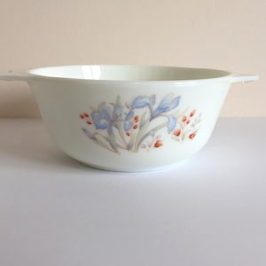 May include: White ceramic bowl with two handles, decorated with a floral pattern of blue irises and red berries. The bowl is round and has a smooth surface, suitable for serving food.