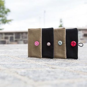 May include: Three small fabric pouches with button closures. The pouches are in beige, black, and brown with different coloured buttons.