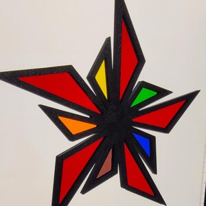 May include: A star-shaped ornament with a black outline and colorful geometric shapes. The star features red, yellow, green, blue, orange, and brown segments. A small black loop is at the top for hanging.