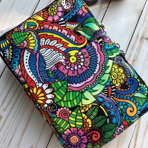 May include: A colorful zippered pouch with a black background and a paisley-like pattern featuring flowers, leaves, and swirls in shades of red, yellow, blue, green, and pink.