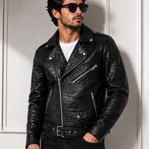 Puede incluir: Una chaqueta de motorista negra con un patrón texturizado de piel de cocodrilo, con una cremallera frontal asimétrica plateada, bolsillos con cremallera en el pecho y los lados, solapas con botones a presión y un cinturón ajustable.