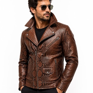 May include: A brown motorcycle jacket featuring a textured snakeskin pattern, a wide notched collar, a diagonal front zip closure, and multiple zipped pockets with silver-toned hardware, worn over a plain black t-shirt and black trousers.