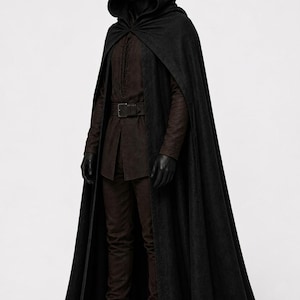 May include: A full-length black hooded cloak worn over a dark brown long-sleeved tunic and matching trousers. The outfit includes a dark brown belt with a rectangular buckle and black gloves, presented on a mannequin against a plain background.