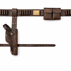 May include: A brown leather gun belt with a holster, cartridge holders, and pouches. The belt features a buckle, brass accents, and a strap for the leg. The leather has a distressed finish.