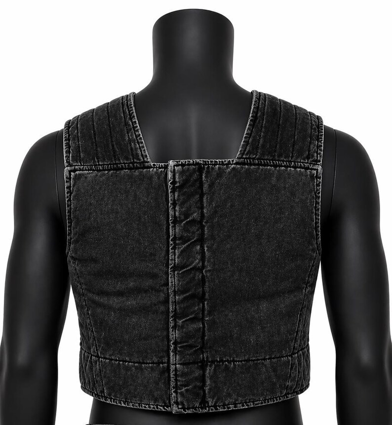 May include: A black denim vest with a square neckline and a cropped fit. The vest features vertical stitching on the shoulders and a central seam down the back. The fabric has a faded, worn appearance.