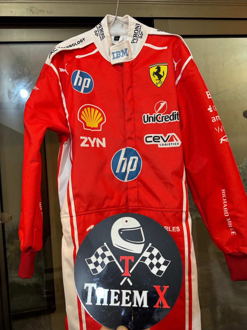 May include: Red racing suit with white detailing, displaying sponsor logos including HP, Shell, and IBM. The suit features a Ferrari emblem and the text "RICHARD MILLE". A black circular sticker with a helmet and checkered flags is attached.