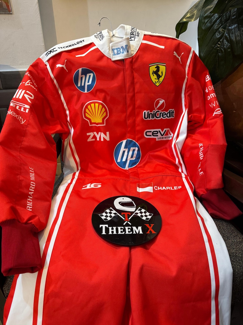 May include: Red racing suit with white stripes and sponsor logos such as HP, Shell, and Unicredit. The Ferrari logo is visible. The suit has the text "THEEM X" on a black oval and the number 16.