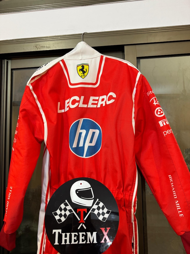 May include: Red racing suit with white detailing, displaying the Ferrari logo and the name "LECLERC". The suit includes the HP logo and the text "RICHARD MILLE". A circular sticker with a helmet and checkered flags is also visible.
