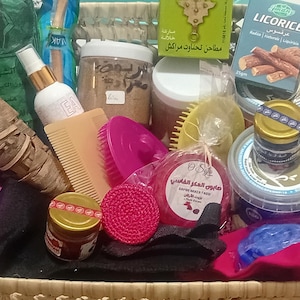 Puede incluir: Una cesta de mimbre llena de varios productos de cuidado personal. Los artículos incluyen frascos, botellas, peines, jabones y una caja de regaliz. Los productos son de varios colores, incluyendo rosa, amarillo y rojo.