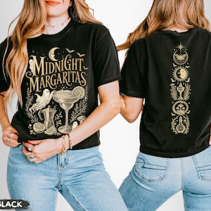 May include: A black t-shirt featuring a gold graphic print. The front displays the text Midnight Margaritas with a ghost, a margarita glass, a coffee pot, and citrus slices. The back shows a vertical column of celestial and occult symbols.