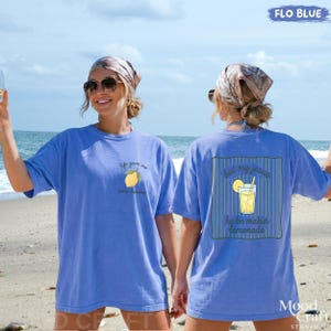 Op de afbeelding: Een korenblauwe t-shirt met een kleine citroenafbeelding en de tekst "life gave me some lemons" op de linkerborst, en een grotere afbeelding op de achterkant met een glas limonade en de tekst "but my jesus he be makin lemonade".