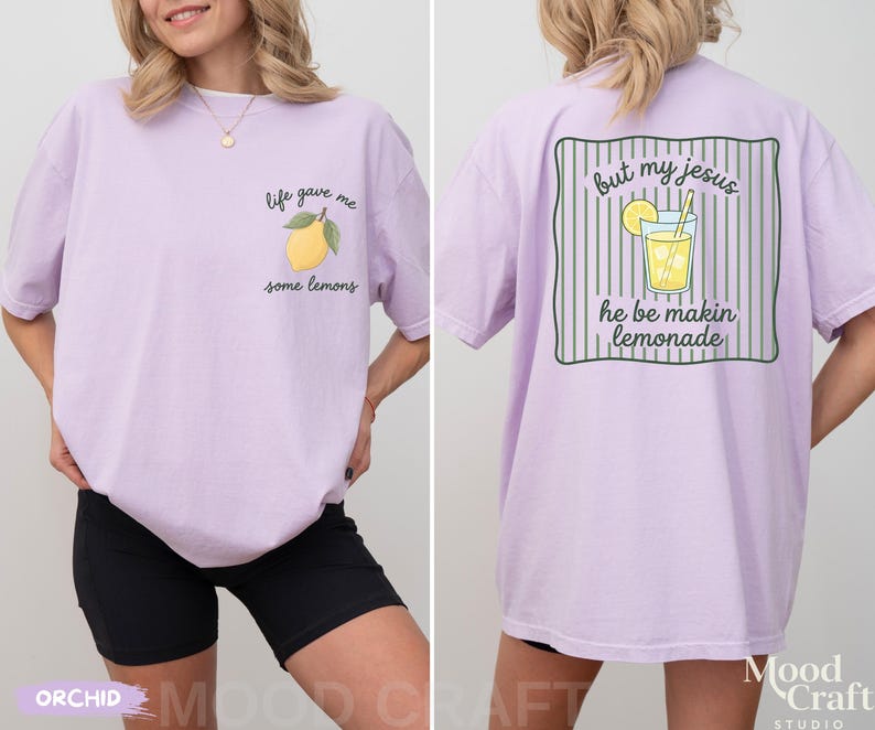 Op de afbeelding: Een lichtpaars t-shirt met een kleine gele citroenafbeelding op de voorkant met de tekst "life gave me some lemons". De achterkant toont een grotere afbeelding van een glas limonade met de tekst "but my jesus he be makin lemonade".