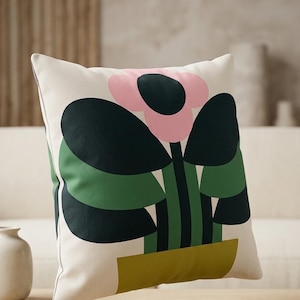 May include: A square cushion with a bold floral pattern. The design includes a pink flower with a black centre, dark green leaves, and a yellow-green pot on a cream background. The cushion is square in shape.