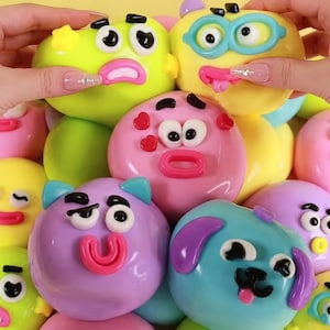Peut inclure: Une collection de jouets sensoriels ronds, souples et colorés, présentant divers visages de dessins animés avec des yeux, des bouches et des oreilles en plastique en relief. Les jouets sont vert citron, jaune vif, rose pastel, violet et bleu clair.