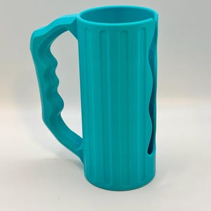 May include: A teal-colored, cylindrical mug with a large handle. The mug has vertical ridges along its body and a curved cutout on one side. The handle is designed for a comfortable grip. The mug is made of a solid, opaque material.