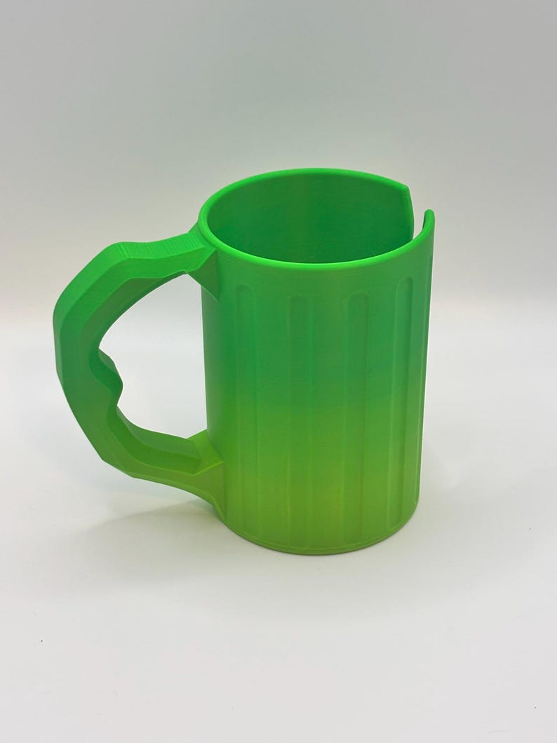 May include: A bright green mug with a large handle. The mug has vertical lines on the side and a curved top. The handle is thick and angular, matching the mug's vibrant color. The mug is made of plastic.