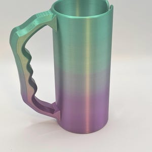 May include: A tall, cylindrical mug with a large handle. The mug features a gradient color scheme, transitioning from green at the top to purple at the bottom. The handle is a matching gradient of green and purple.