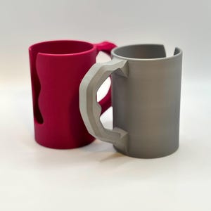 May include: A set of three ceramic mugs with a speckled, cream-colored glaze. Each mug features a different hand-painted design: a blue and green leaf, a yellow flower, and a red berry. The mugs have a simple, rounded shape.