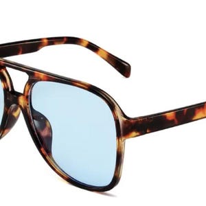 May include: Aviator-style sunglasses with a tortoiseshell frame and light blue lenses. The sunglasses have a double bridge and thick temples. The lenses are a light blue color, and the frame has a brown and black pattern.