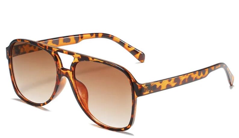 May include: Brown gradient lens sunglasses with a tortoise shell pattern on the frames and arms. The sunglasses have a double bridge design and a classic aviator shape. The lenses transition from a darker brown at the top to a lighter brown at the bottom.