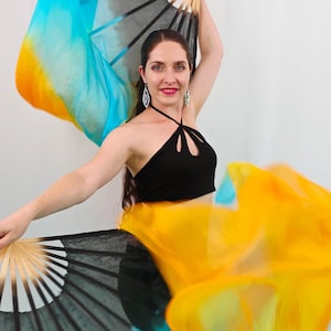 May include: A pair of dance fans featuring long, flowing silk fabric in a gradient of black, bright blue, and yellow. The fans have light-colored wooden ribs and are extended to show the vibrant color transition across the lightweight material.