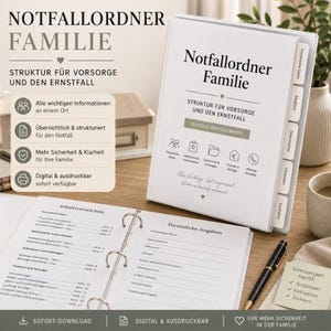 以下が含まれることがあります： 「Notfallordner Familie」と書かれた白いバインダー。個人データ、医療情報、財務情報用のタブが付いています。バインダーは開いており、罫線入りのページが表示されています。黒いペンとカップが木製の表面にあります。