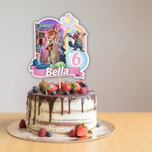 May include: A Zootopia themed cake topper featuring characters Nick Wilde, Judy Hopps, and a beaver, with a rainbow, balloons, the number 6, and the name Bella printed on a pink banner, displayed on a round cake with chocolate ganache and berries.