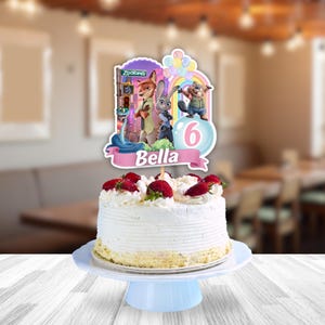 May include: A round white frosted cake topped with fresh strawberries and whipped cream, featuring a Zootopia-themed cake topper with characters, a rainbow, balloons, the number 6, and a pink banner with the name Bella printed in white.