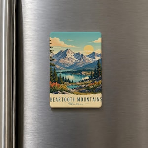 May include: A rectangular magnet featuring a scenic landscape of the Beartooth Mountains in Montana. The image depicts snow-capped mountains, a lake, and a sunset. Text at the bottom reads "BEARTOOTH MOUNTAINS - Montana."