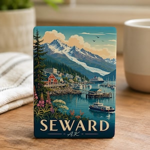 May include: A rectangular magnet featuring a colorful illustration of Seward, Alaska. The scene depicts a coastal town with red buildings, a harbor with boats, a cruise ship, and snow-capped mountains under a blue sky. The text SEWARD AK is at the bottom.