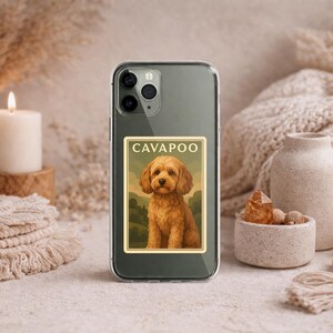 May include: A clear phone case with a rectangular sticker featuring a Cavapoo dog illustration. The dog is light brown with a fluffy coat, set against a landscape background. The word "CAVAPOO" is at the top of the sticker.