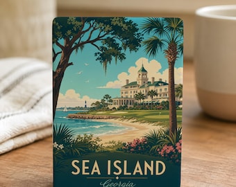 May include: A rectangular Sea Island, Georgia, souvenir featuring a coastal landscape illustration. The artwork depicts a large white building, palm trees, and a beach under a blue sky. The text "SEA ISLAND Georgia" is prominently displayed.