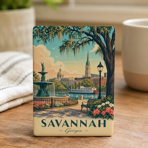 A decorative souvenir magnet depicting a scenic view of Savannah, Georgia, with a fountain, trees, and buildings in the background.