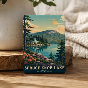 May include: A rectangular magnet featuring a landscape illustration of Spruce Knob Lake in West Virginia. The scene depicts a calm blue lake, a white building, evergreen trees, rocky shores, orange flowers, and a mountain under a sunlit sky.