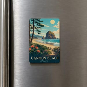May include: A rectangular magnet featuring a scenic illustration of Cannon Beach, Oregon. The artwork depicts a beach with a large rock formation in the ocean, a path, and the text "Cannon Beach Oregon". The sky is blue with a yellow sun.