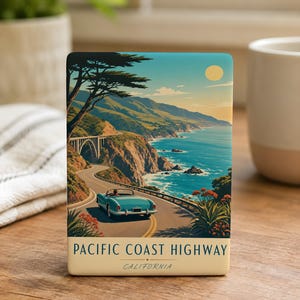 May include: A rectangular decorative tile featuring a scenic illustration of the Pacific Coast Highway in California. The image depicts a teal convertible driving along a coastal road, with a bridge, ocean, and mountains under a sunny sky. The text "PACIFIC COAST HIGHWAY CALIFORNIA" is at the bottom.