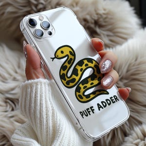 May include: Clear phone case featuring a yellow and black snake illustration with the text "PUFF ADDER". The case is transparent, allowing the phone's design to show through. The snake design is a cartoon style.
