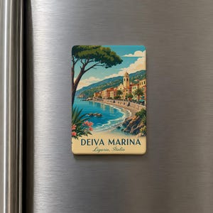 May include: A rectangular refrigerator magnet featuring a colorful illustration of the coastal town of Deiva Marina in Liguria, Italy. The scene depicts a blue sea, a sandy beach, palm trees, and buildings, with the text DEIVA MARINA Liguria, Italia.
