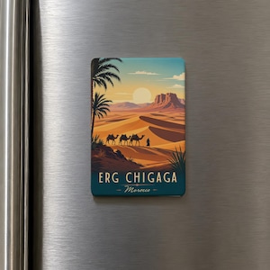 May include: A rectangular magnet featuring a desert landscape with camels, palm trees, and a sunset. The text "ERG CHIGAGA - Morocco" is displayed at the bottom. The magnet is attached to a stainless steel surface.