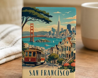 May include: A rectangular ceramic tile featuring a San Francisco scene. The image includes the Golden Gate Bridge, a cable car, and Victorian houses. The text "SAN FRANCISCO CA" is displayed at the bottom. The tile is set on a wooden surface.