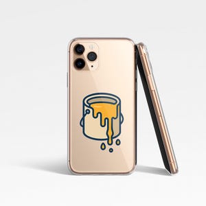 May include: A clear phone case with a gold-colored phone inside, featuring a cartoon illustration of a paint can with yellow paint dripping down. A second phone leans against the first. The design is outlined in blue.