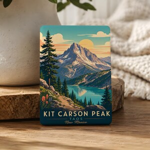 May include: A rectangular magnet featuring a scenic landscape of Kit Carson Peak in Taos, New Mexico. The artwork depicts a mountain range, a lake, and evergreen trees under a sunset sky. The magnet has the text "KIT CARSON PEAK TAOS New Mexico".